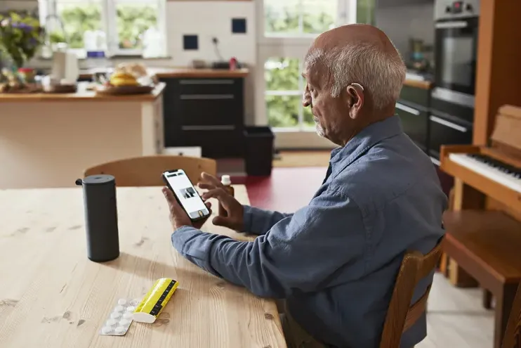一个戴着助听器的老人坐在桌边玩智能手机